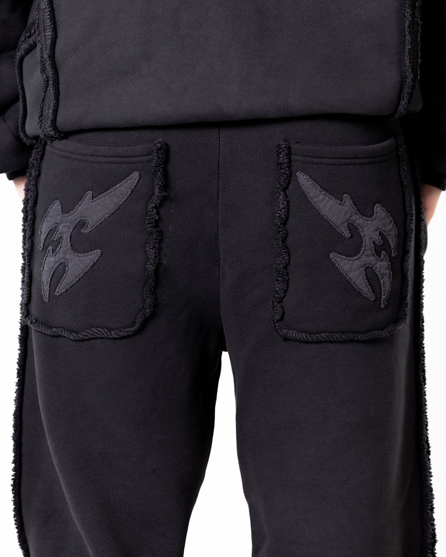 Detailaufnahme der Gesäßtaschen einer schwarzen Hose mit applizierten Flammenmotiven und ausgefransten Kanten.